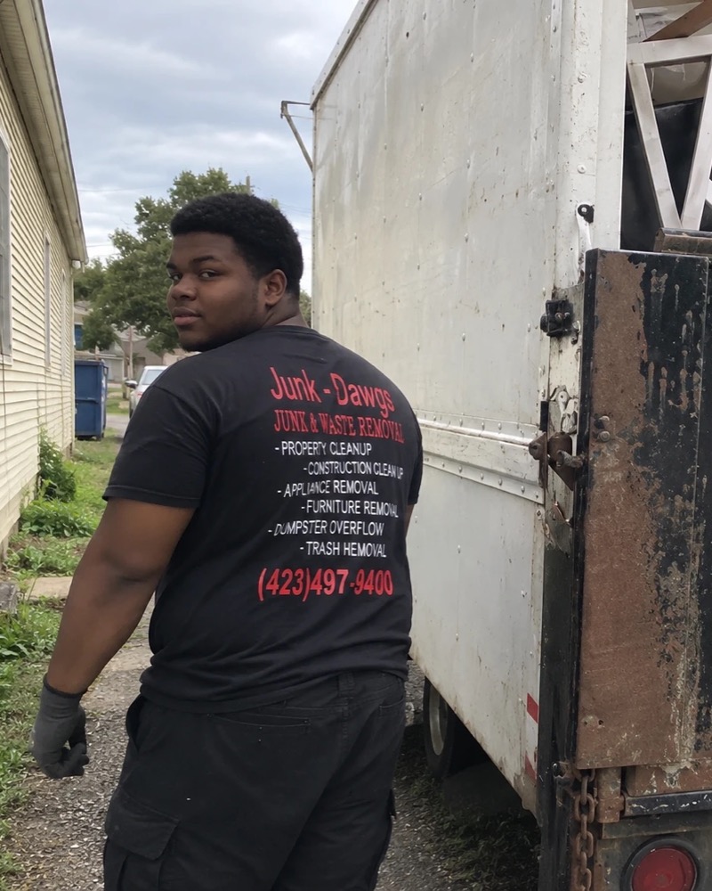 A Junk Dawgs crew member in the black company shirt, standing by the loaded box truck at a job